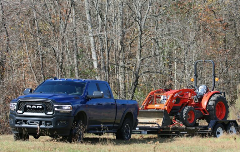 a blue pickup truck towing a red tractor